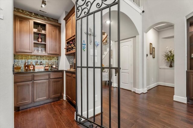 indoor bar featuring arched walkways, dark wood-type flooring, decorative backsplash, and baseboards