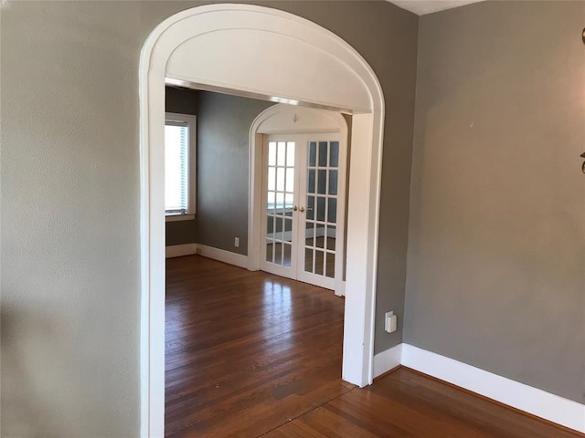 spare room featuring french doors, arched walkways, wood finished floors, and baseboards