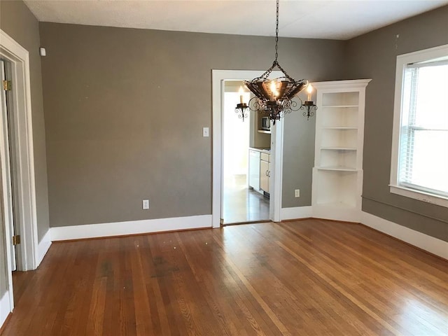 unfurnished dining area with hardwood / wood-style flooring, a chandelier, and baseboards
