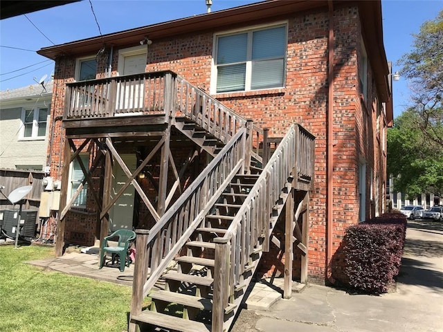 rear view of property with brick siding, stairway, a deck, and a yard