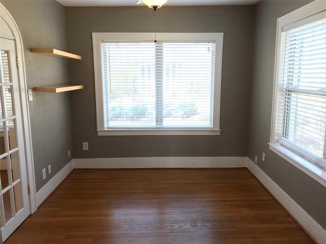 unfurnished dining area with healthy amount of natural light, wood finished floors, and baseboards