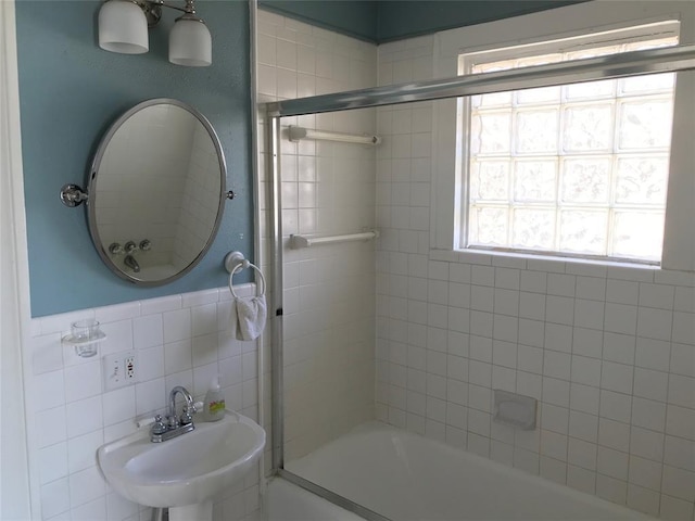 full bathroom with a sink, bath / shower combo with glass door, and tile walls
