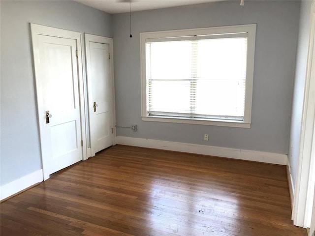 unfurnished bedroom with wood finished floors, baseboards, and multiple closets