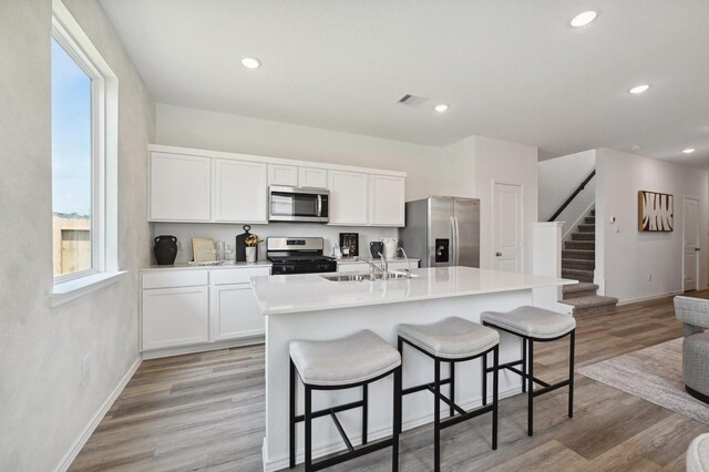 16602 Bobal Path, Houston, TX 77090 - kitchen featuring stainless steel appliances, a sink, a breakfast bar area, white cabinetry, and an island with sink