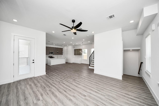 unfurnished living room featuring light wood-style flooring, ceiling fan, recessed lighting, stairs, and baseboards