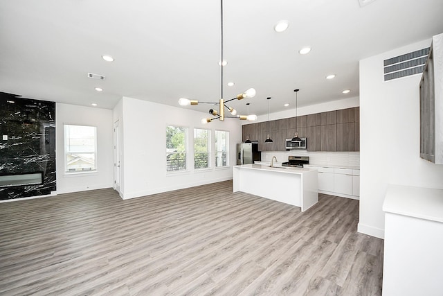 kitchen with stainless steel appliances, modern cabinets, a sink, a kitchen island with sink, and light countertops