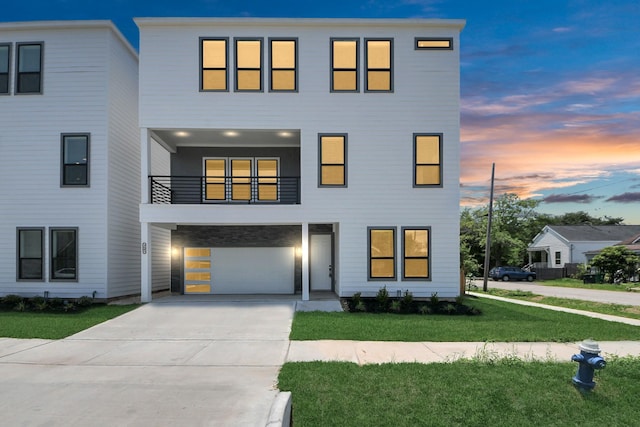 view of front of home with an attached garage, concrete driveway, a yard, and a balcony