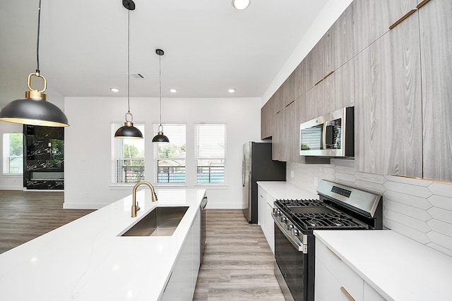 kitchen featuring appliances with stainless steel finishes, a sink, modern cabinets, light countertops, and backsplash