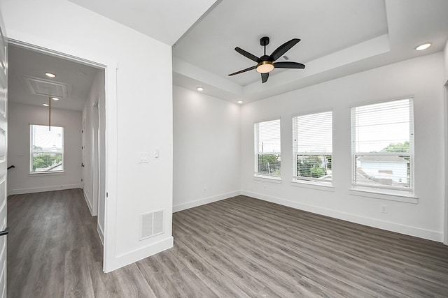 empty room featuring attic access, ceiling fan, a tray ceiling, wood finished floors, and recessed lighting