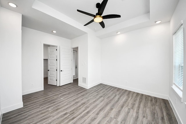 unfurnished bedroom with wood finished floors, baseboards, recessed lighting, and a raised ceiling