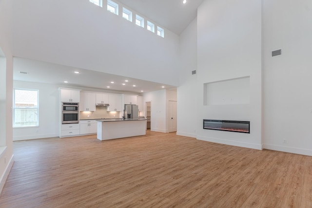 3203 Hemingway Dr, Montgomery, TX 77356 - unfurnished living room featuring light wood-type flooring, baseboards, recessed lighting, a glass covered fireplace, and a towering ceiling