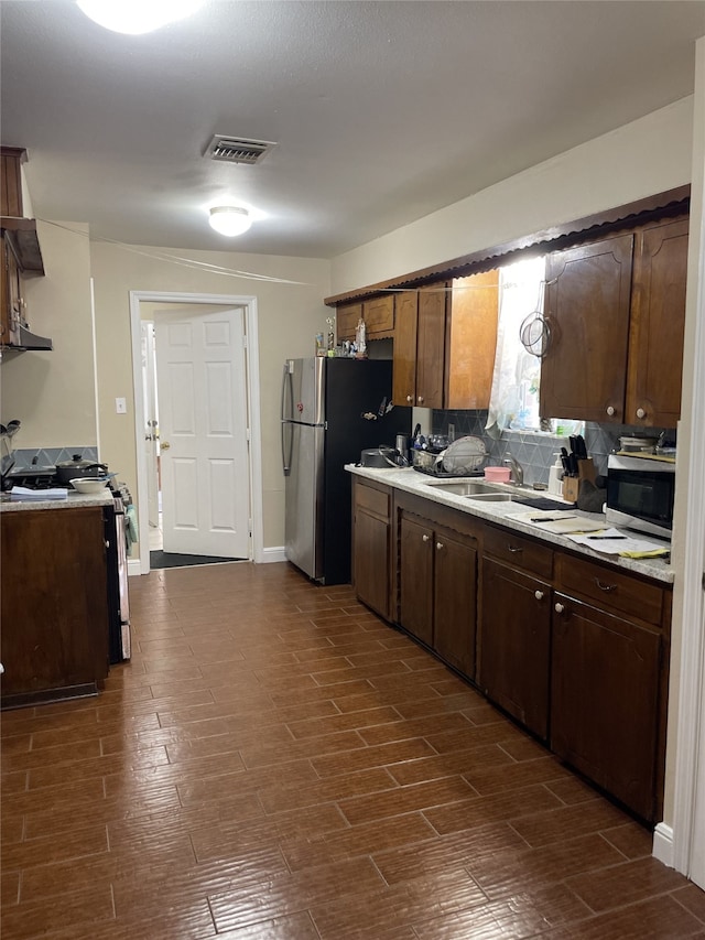 kitchen featuring a sink, stainless steel appliances, light countertops, tasteful backsplash, and dark wood-style floors