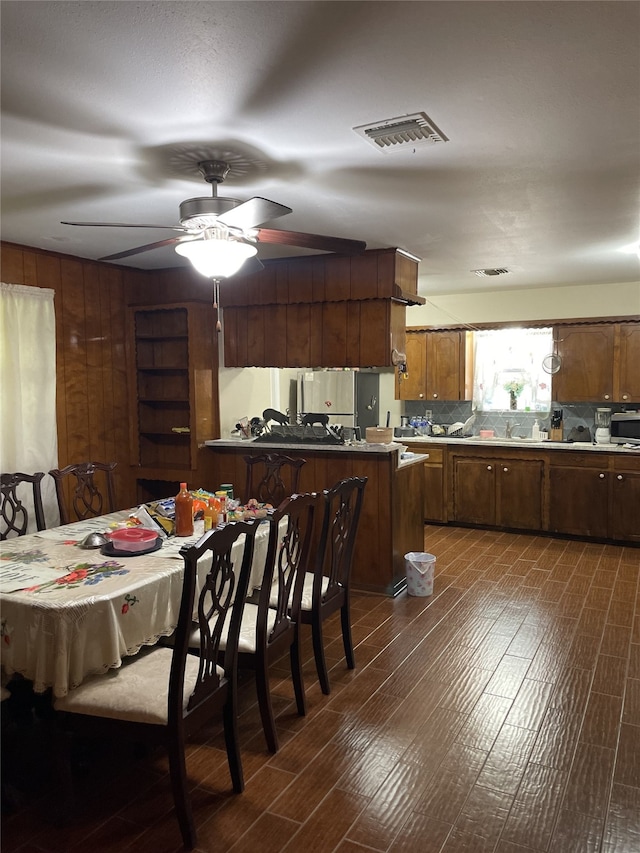kitchen with dark wood-style flooring, wood walls, a ceiling fan, tasteful backsplash, and a peninsula