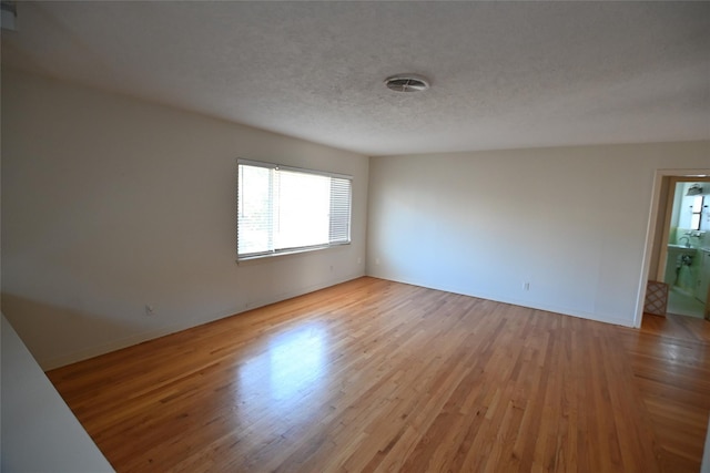 empty room with light wood-style flooring, baseboards, and a textured ceiling