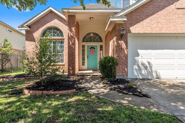view of exterior entry with brick siding, fence, a garage, and concrete driveway