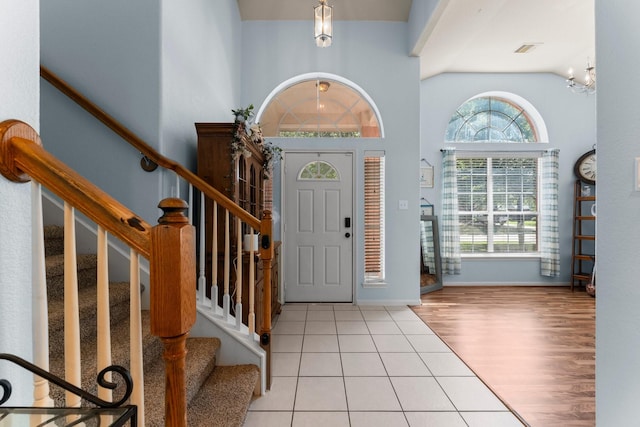 entryway featuring light tile patterned floors, a high ceiling, stairs, a chandelier, and baseboards