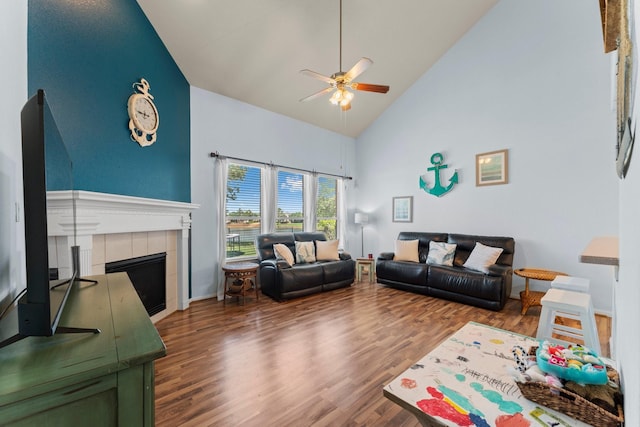 living room with high vaulted ceiling, wood finished floors, ceiling fan, a tile fireplace, and baseboards