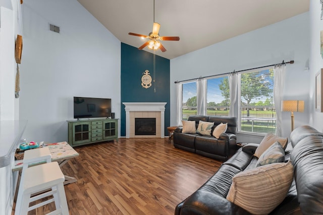 living area with high vaulted ceiling, ceiling fan, wood finished floors, and a tiled fireplace