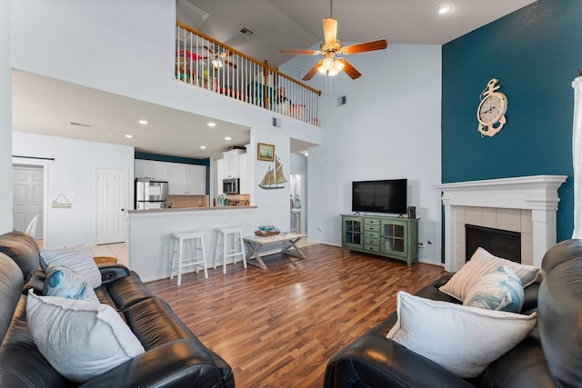 living room featuring a ceiling fan, light wood finished floors, a high ceiling, recessed lighting, and a fireplace