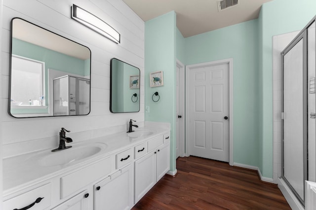 bathroom with a stall shower, wood finished floors, double vanity, and baseboards