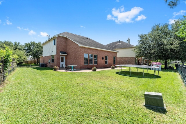 rear view of property featuring a trampoline, a patio, brick siding, and central AC unit