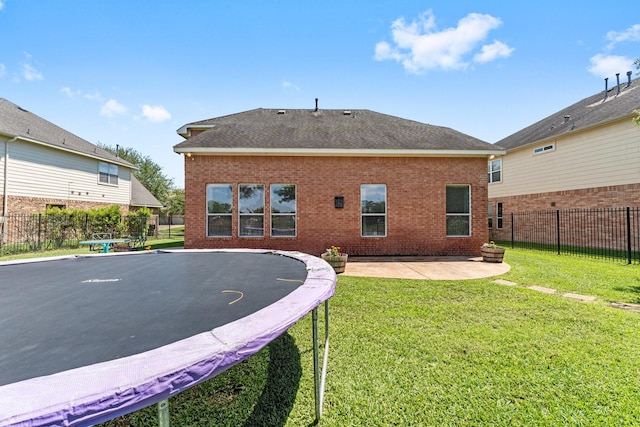 back of property with a trampoline, brick siding, a patio, and a shingled roof