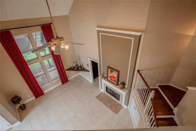 unfurnished living room featuring ceiling fan, baseboards, stairway, a tile fireplace, and light tile patterned floors