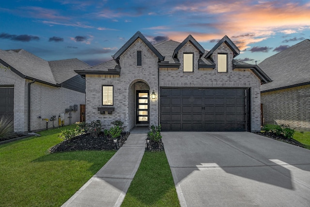 french provincial home with concrete driveway, a front lawn, a garage, brick siding, and roof with shingles