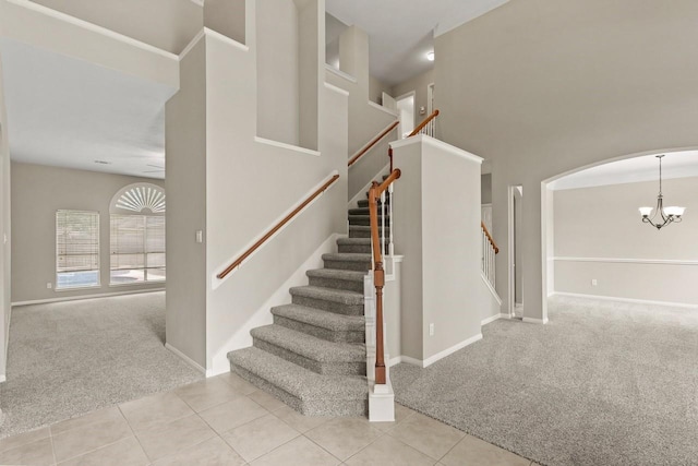 stairs with carpet flooring, a chandelier, a towering ceiling, tile patterned floors, and baseboards