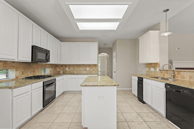 kitchen with black appliances, a sink, arched walkways, decorative backsplash, and a center island