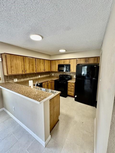 11957 Bob White Dr Unit 863, Houston, TX 77035 - kitchen featuring black appliances, brown cabinetry, a peninsula, a sink, and a textured ceiling