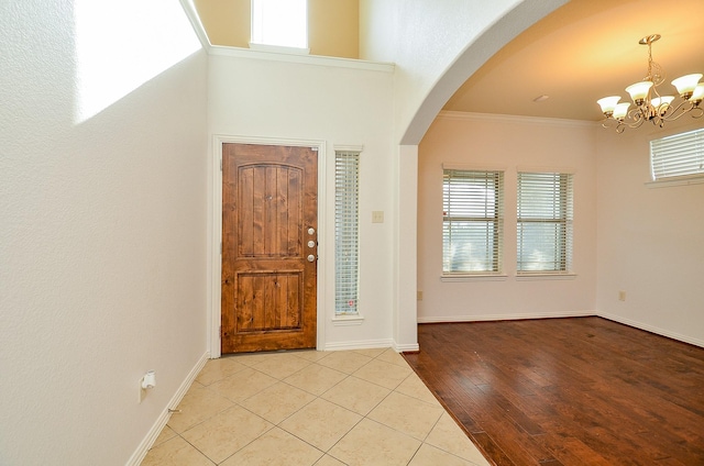 tiled entrance foyer with a chandelier, arched walkways, baseboards, and ornamental molding