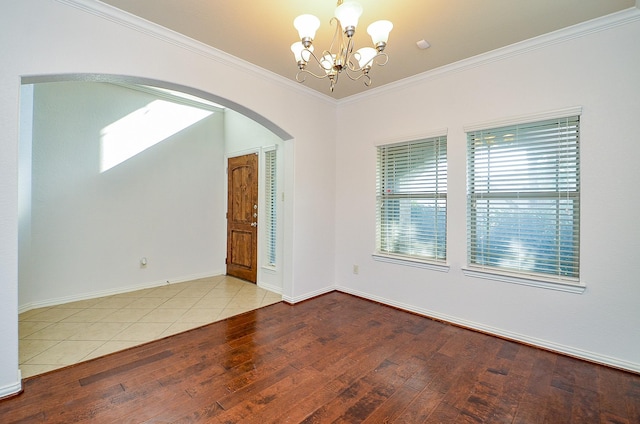 empty room featuring arched walkways, a chandelier, hardwood / wood-style flooring, crown molding, and baseboards