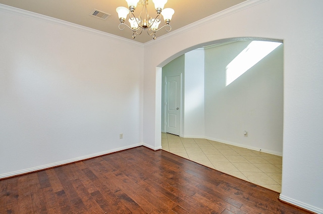empty room featuring arched walkways, hardwood / wood-style flooring, ornamental molding, a chandelier, and baseboards