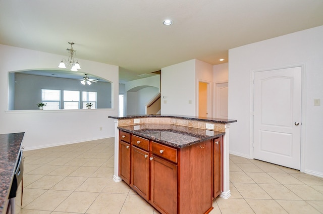 kitchen with arched walkways, light tile patterned floors, a chandelier, dark stone countertops, and pendant lighting