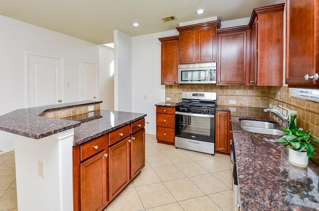 kitchen featuring appliances with stainless steel finishes, a sink, light tile patterned floors, tasteful backsplash, and dark stone countertops