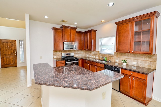 kitchen featuring appliances with stainless steel finishes, light tile patterned flooring, tasteful backsplash, a sink, and dark stone counters