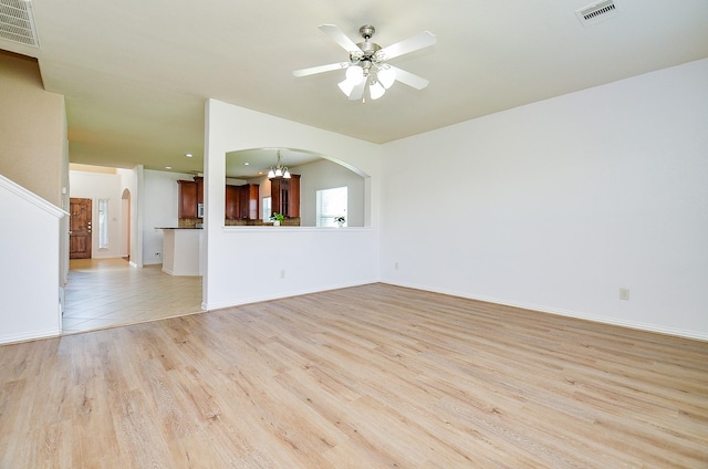 unfurnished living room with light wood-style flooring, ceiling fan, arched walkways, and baseboards
