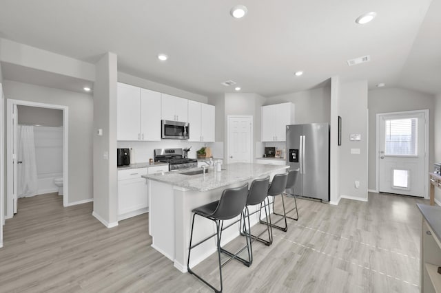 8230 Red Spruce St, Magnolia, TX 77354 - kitchen featuring appliances with stainless steel finishes, a breakfast bar, white cabinetry, an island with sink, and lofted ceiling