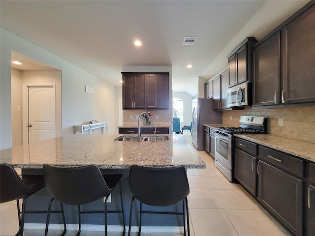 4931 Marina Shores Ct, Katy, TX 77493 - kitchen featuring stainless steel appliances, a sink, decorative backsplash, light stone countertops, and a breakfast bar area