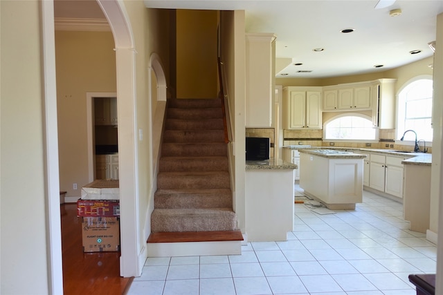 kitchen with a sink, arched walkways, tasteful backsplash, a center island, and light stone counters
