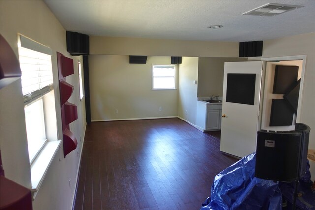 unfurnished living room with dark wood-type flooring, a sink, a textured ceiling, and baseboards