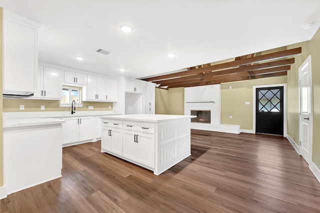 kitchen featuring wood finished floors, a fireplace, white cabinetry, light countertops, and a center island