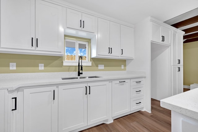 kitchen featuring a sink, white cabinetry, light wood-style flooring, and light stone counters