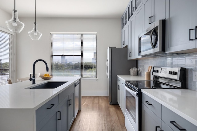 kitchen with stainless steel appliances, a sink, gray cabinetry, and light countertops