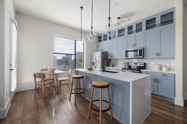 kitchen featuring stainless steel appliances, a sink, a kitchen island with sink, tasteful backsplash, and dark wood finished floors