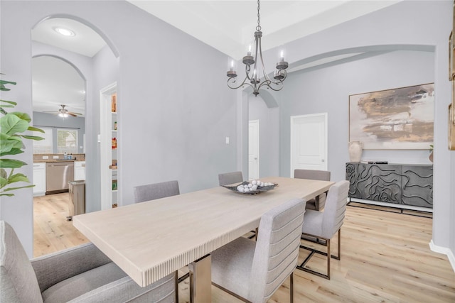 dining area with arched walkways, light wood-type flooring, and a ceiling fan