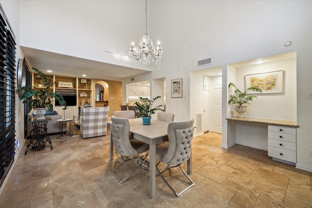 dining area featuring stone tile floors, a towering ceiling, arched walkways, built in features, and baseboards