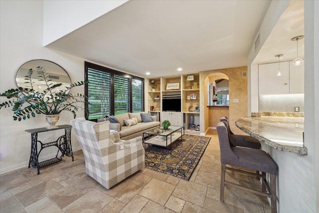 living area with stone tile floors, baseboards, built in features, recessed lighting, and arched walkways
