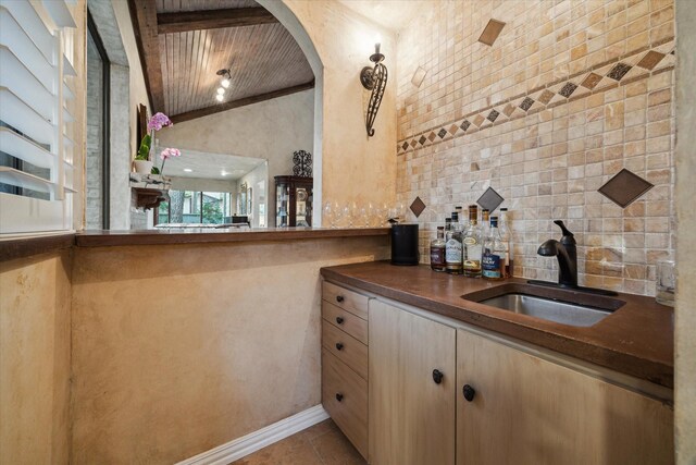 bar area with a sink, arched walkways, backsplash, and tile patterned floors